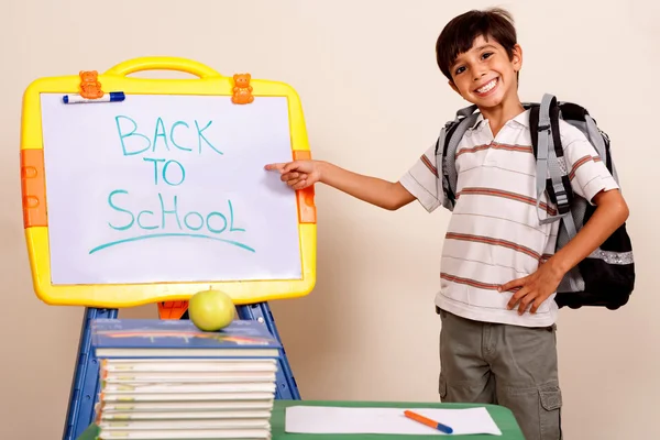 Uśmiechnięty chłopiec szkoły wskazując na pokładzie biały — Zdjęcie stockowe