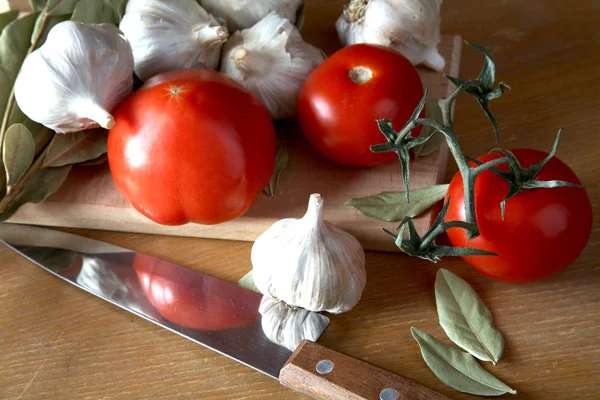 Tomater vitlök och lagerblad grenar på ett bord — Stockfoto