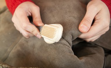 Woman cleaning a sheepskin with whisk broom clipart