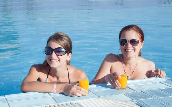 Girls relaxing in tropical pool with orange juice — Stock Photo, Image
