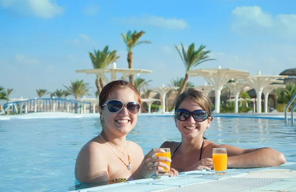 Chicas relajándose en la piscina tropical con jugo de naranja — Foto de Stock