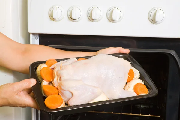 Женщина кладет курицу в духовку — стоковое фото