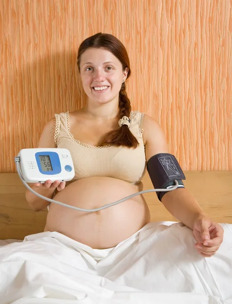 怀孕的女人在家里的床上测量血压 — 图库照片