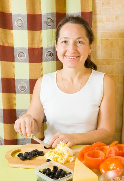 成熟した女性は 彼女のキッチンでまな板の上にオリーブをスライスします ぬいぐるみトマトの調理のシリーズの段階の参照してください — ストック写真