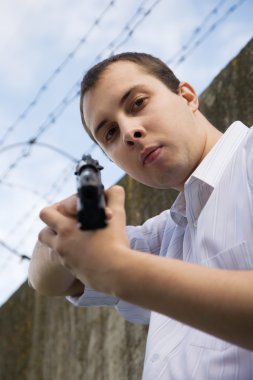 Young man aiming a black gun against the prison wall clipart