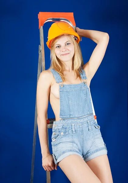 性感的女孩的工作服和安全帽上梯子在蓝色 — 图库照片