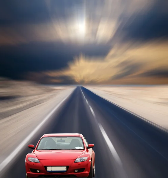 stock image Red car on desert road under cloudy sky