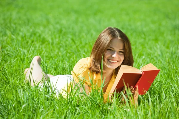 本を読んで楽しんで草原で草の上に横たわってリラックスする少女 — ストック写真