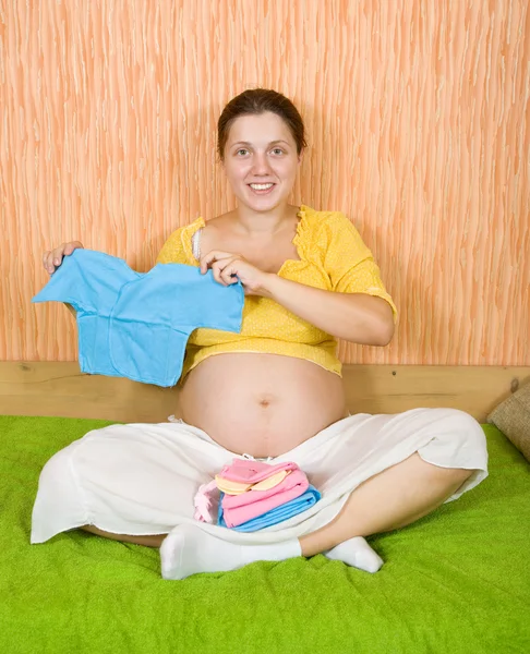 Pregnant woman with baby's clothes — Stock Photo, Image