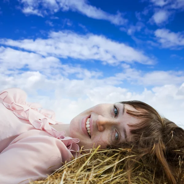 空に対して新鮮な干し草ベールで休んでの女の子 — ストック写真