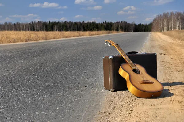 Zavazadla a kytara na prázdné silnici — Stock fotografie