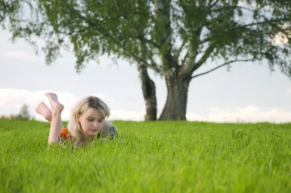 Giovane bella donna posa sul campo verde e legge — Foto Stock
