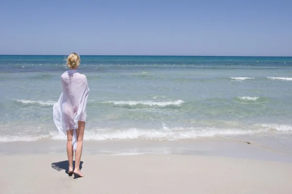 stock image Beautiful young girl in white walking on the beach