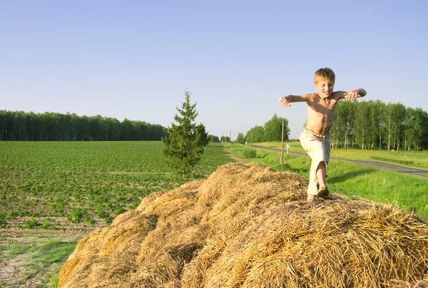 Boy jump on a hayrick and throw a straw — Stock Photo, Image