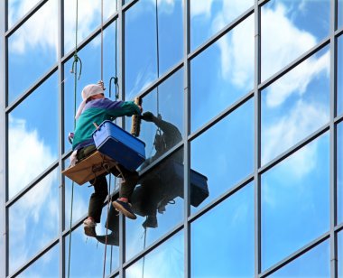 Window cleaner hanging on rope at work on skyscraper clipart
