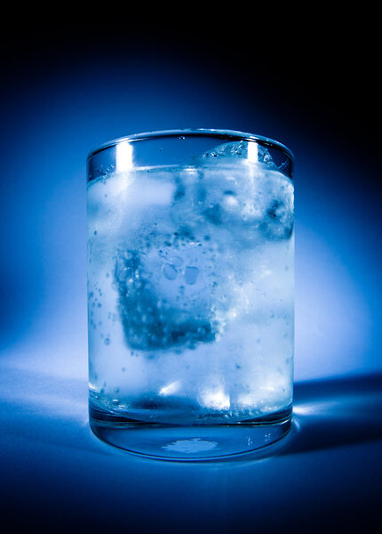 Misted over glass of water with ice on a dark blue