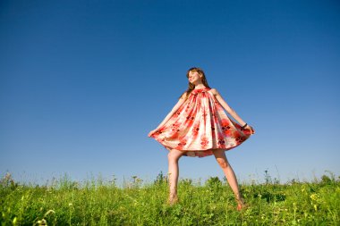 mutlu kız bir çayır kaçan. Kırmızı elbise ve kırmızı ayakkabılar. Mavi gökyüzü fonunda.