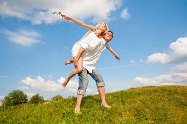 Happy young couple jumping in sky above a green meadow clipart