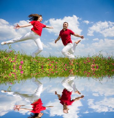 Happy Young Couple - team is jumping in the sky above a green meadow clipart