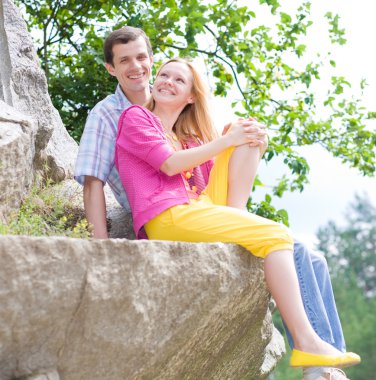 Casual happy couple sits on a rock clipart