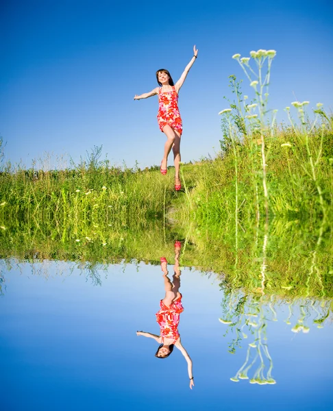 在一片草地上逃离的快乐女孩 在红色礼服和红色的鞋子 蓝蓝的天空的背景 — 图库照片