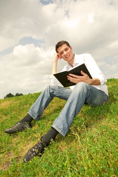 Szczęśliwy człowiek czytając książkę siedzi na zielonej trawie — Zdjęcie stockowe