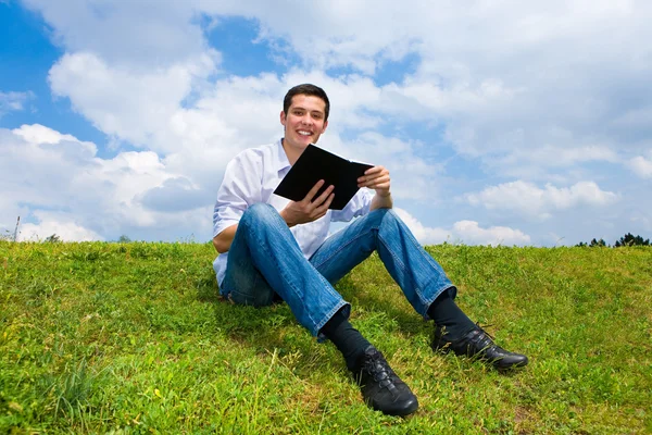 Young man sit in the park enjoying the fresh air and reading a b — Stock Photo, Image