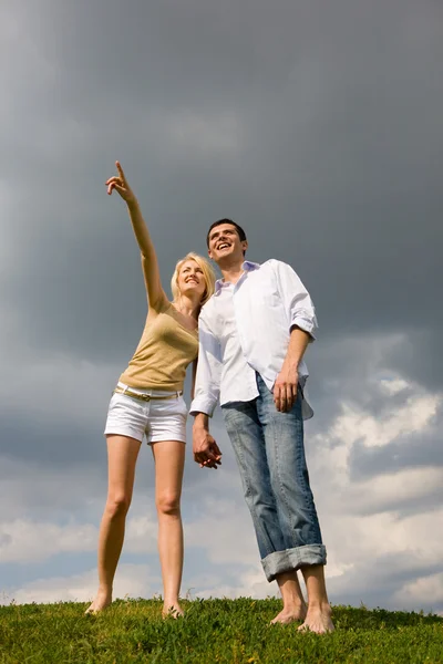 快乐的年轻夫妇看到上面一片绿色的草地的东西 男人用手给看点东西 — 图库照片