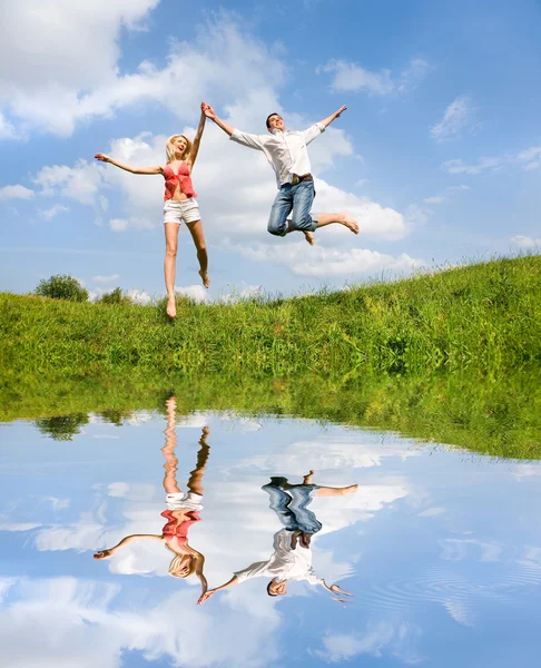 Счастливая молодая пара - прыгает в небе над зеленой горкой — стоковое фото