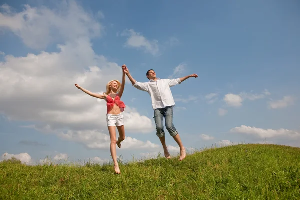 Jovem casal feliz pulando no céu acima de um prado verde — Fotografia de Stock