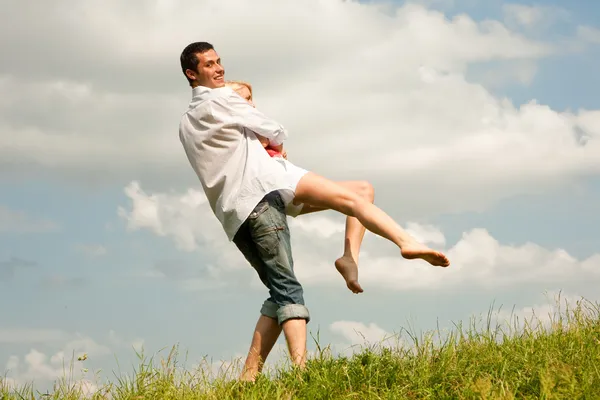 Jovem casal feliz pulando no céu acima de um prado verde — Fotografia de Stock