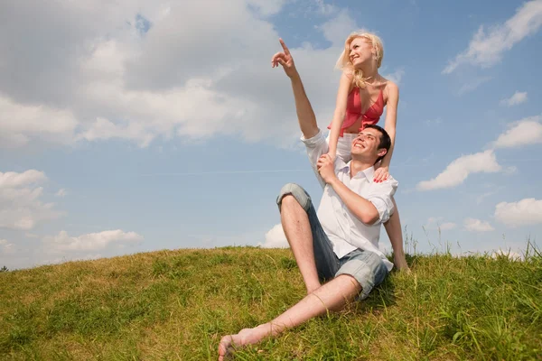 Jovem casal feliz no céu acima de um prado verde — Fotografia de Stock