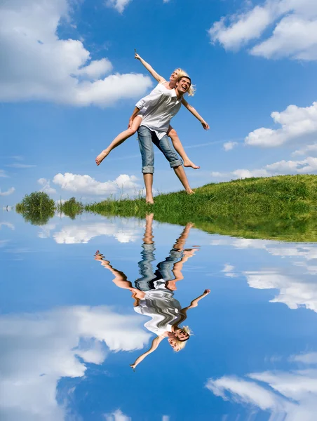 Щаслива молода пара стрибає в небі над зеленим лугом — стокове фото