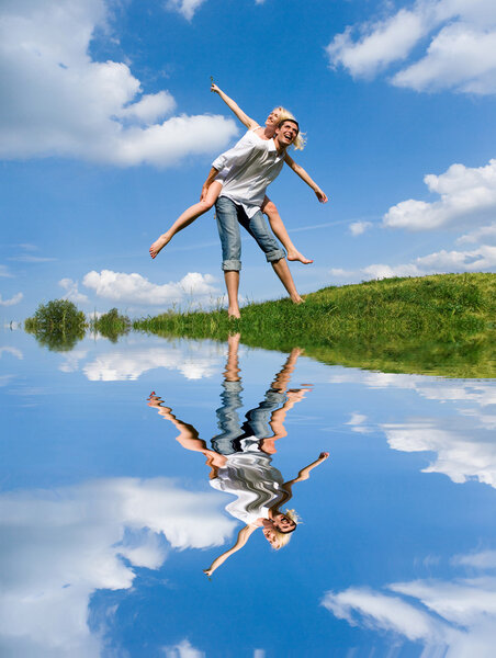 Happy Young Couple - jumping in the sky above a green meadow