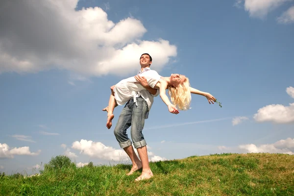 Feliz joven pareja saltando en el cielo sobre un prado verde — Foto de Stock