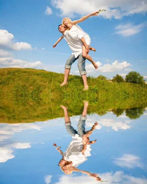 Feliz joven pareja saltando en el cielo sobre un prado verde —  Fotos de Stock