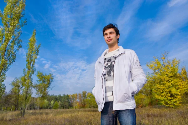 Lachende jonge man tegen de achtergrond van de hemel en bomen — Stockfoto