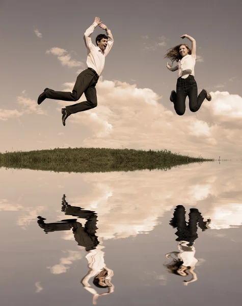 Gelukkige lachende paar springen in blauwe hemel. weerspiegeld in water — Stockfoto