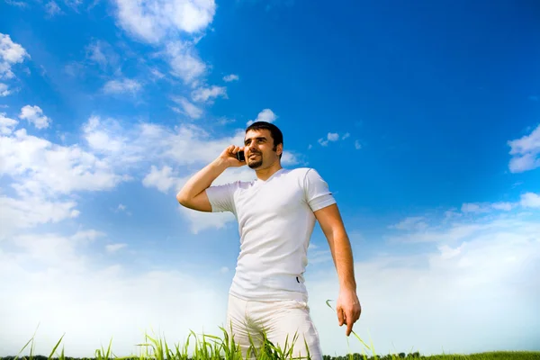 Człowiek na telefon w polu pod błękitne niebo. w białej sukni — Zdjęcie stockowe