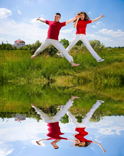 Boldog, fiatal pár - csapat jumping az égen fent egy zöld nekem — Stock Fotó