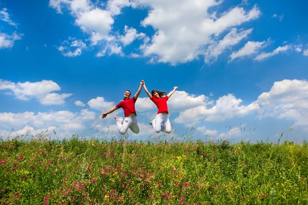 Glückliches junges Paar - Team springt in den Himmel über einem grünen Ich — Stockfoto