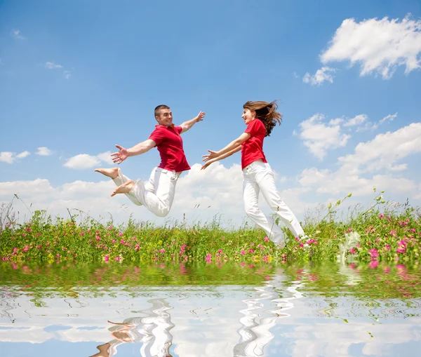 Gelukkige Lachende Paar Springen Hemel Boven Een Groene Weide Weerspiegeld — Stockfoto