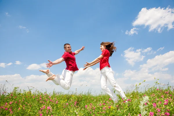 Joyeux couple souriant sautant dans le ciel au-dessus d'une prairie verte — Photo