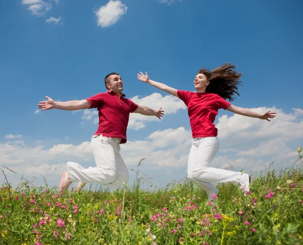 Happy smiling couple jumping in sky above a green meadow — Stock Photo, Image