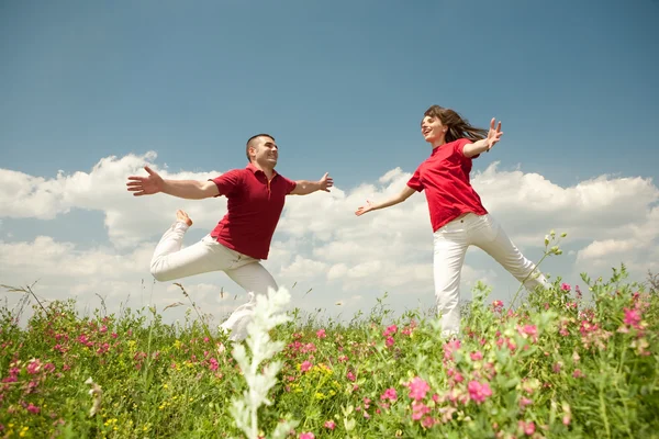 Feliz pareja sonriente saltando en el cielo sobre un prado verde —  Fotos de Stock
