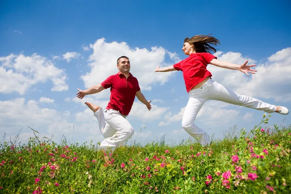 Glückliches junges Paar - Team springt in den Himmel über einem grünen Ich — Stockfoto