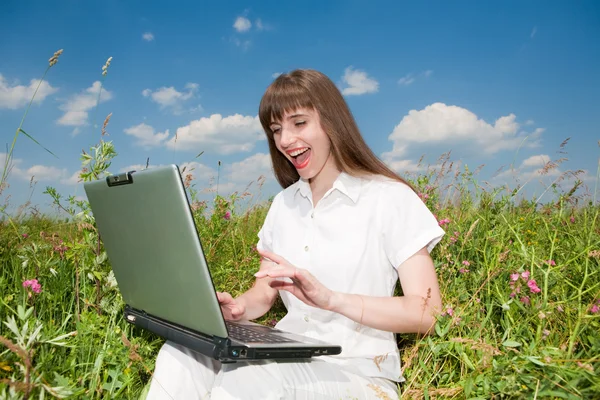 Young woman sitting on the grass field with a laptop. Against th — Stock Photo, Image