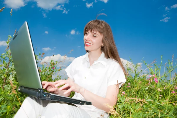 Щаслива молода жінка на полі трави з ноутбуком — стокове фото