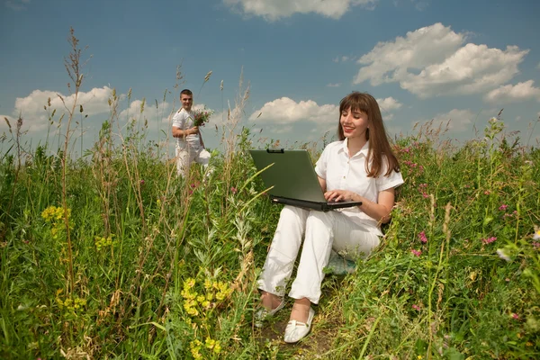 Щаслива молода жінка на трав'яному полі з ноутбуком проти б — стокове фото