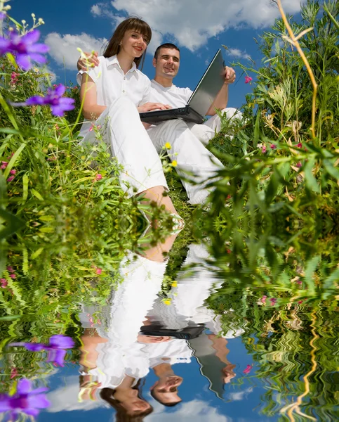 Jeune couple assis sur le champ d'herbe avec un ordinateur portable — Photo